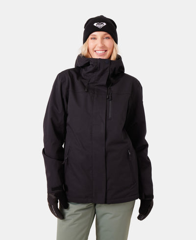 A person wearing a black hooded winter jacket, black gloves, and a black beanie with a white logo, smiling and standing against a white background.