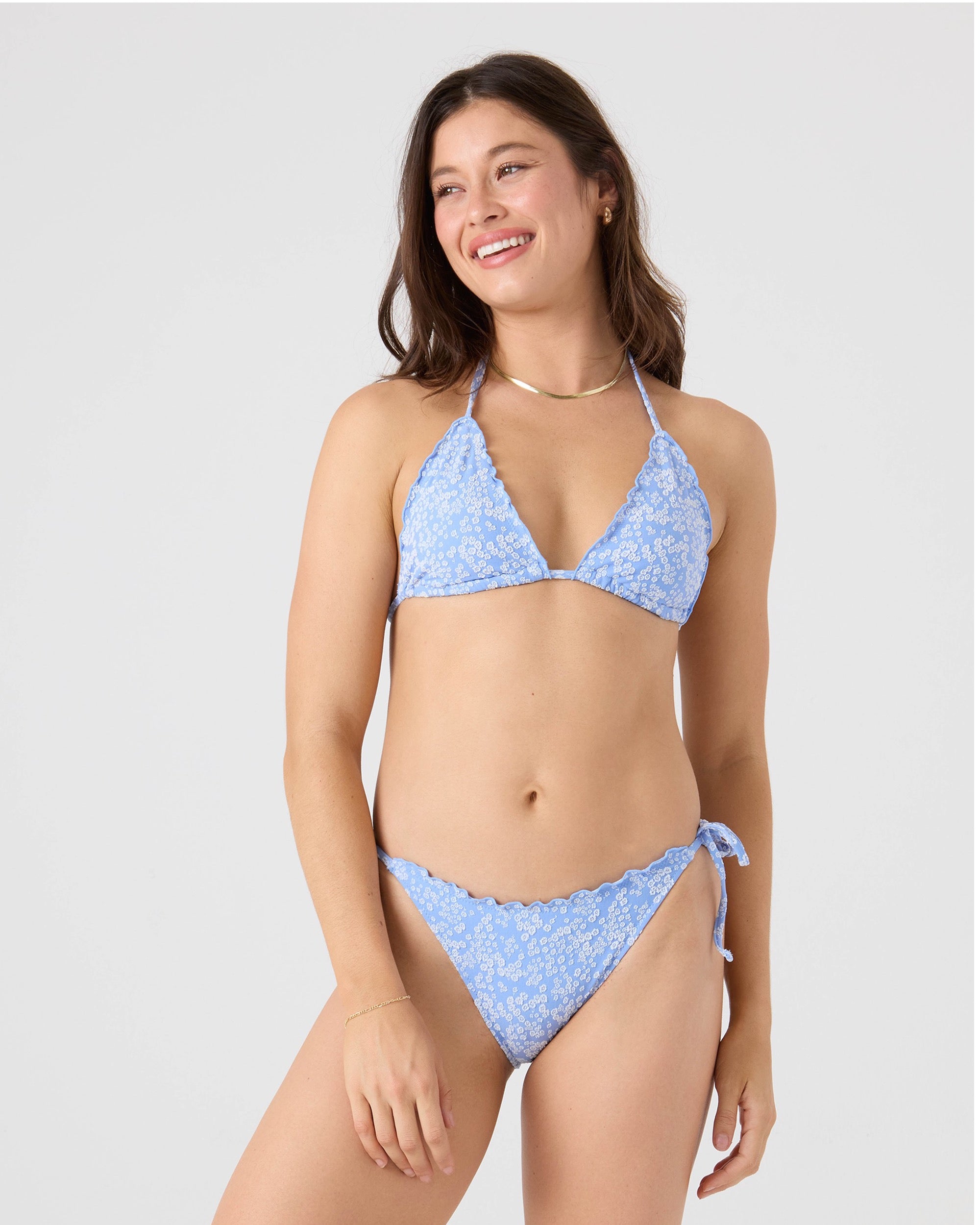 A woman smiles while wearing the Roxy®一分钟极速赛车168开奖结果记录体彩历史号码查询 Margarita Tie Side Cheeky Bikini Bottom in light blue floral with scalloped edges, standing against a plain light background.