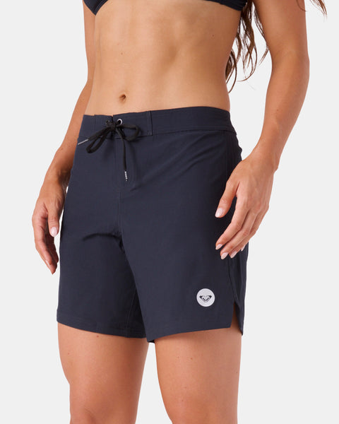 A woman models the Roxy To Dye 7" Boardshort, featuring a black color, tie-front waist, and small white logo on the left leg, shown from mid-torso to sporty mid-thigh against a plain backdrop.