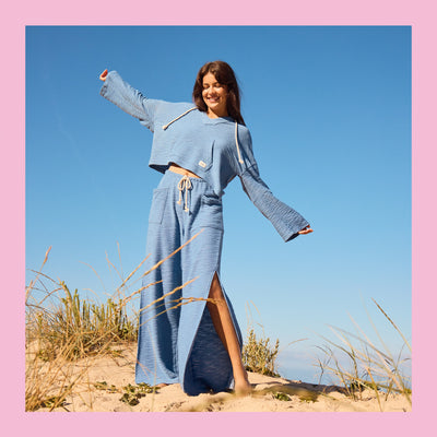 Woman in a blue outfit standing on a beach with a clear blue sky.