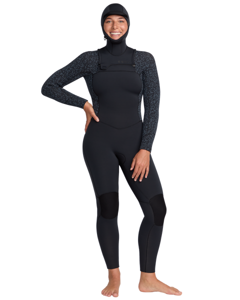 A person stands barefoot, smiling, and wearing the Roxy 5/4mm Swell Natural Hooded Front Zip Wetsuit with subtle patterned sleeves on a plain white background.