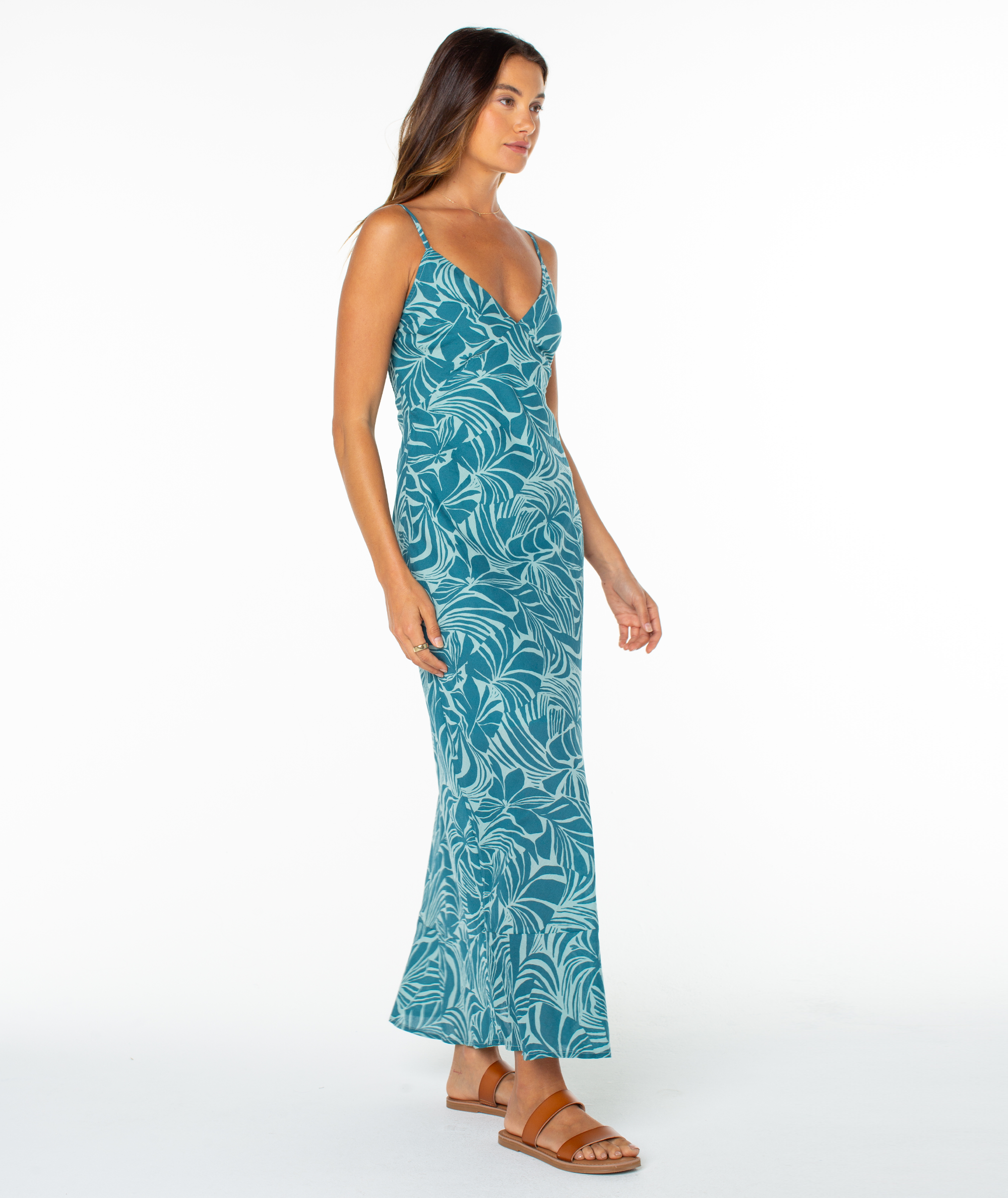 A woman models the Roxy®一分钟极速赛车168开奖结果记录体彩历史号码查询 Lost Paradise Dress—a teal, sleeveless, ankle-length maxi with a leaf print and open back—paired with sandals against a plain white background, gazing slightly to the side.