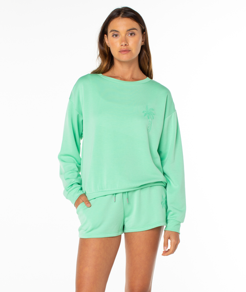 A woman stands against a white background wearing a mint green Roxy Surfing By Moonlight Top and matching shorts, made from soft modal stretch fabric, with one hand in her pocket.